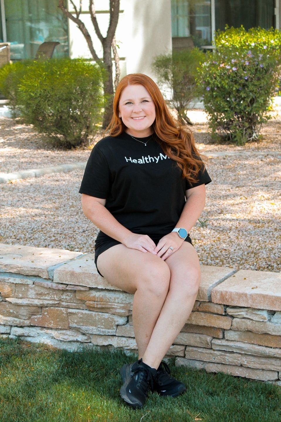 Woman in black shirt sitting on stone wall.